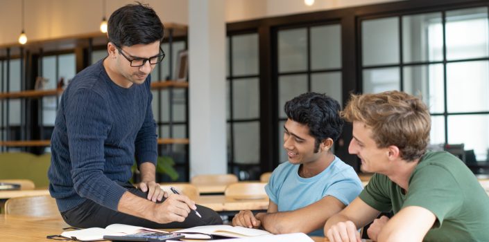 Serious teacher checking assignment of two students. Serious man in glasses pointing pen at notes of two cheerful guys. Education and internship concept